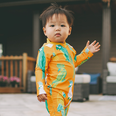 Child wearing an orange and green swimsuit with parrot pattern outdoors.
