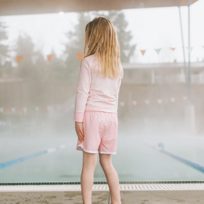 Person wearing a pink outfit standing in front of a pool.