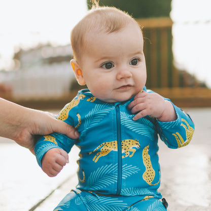 Baby wearing a blue and yellow swimsuit sitting on a ledge.