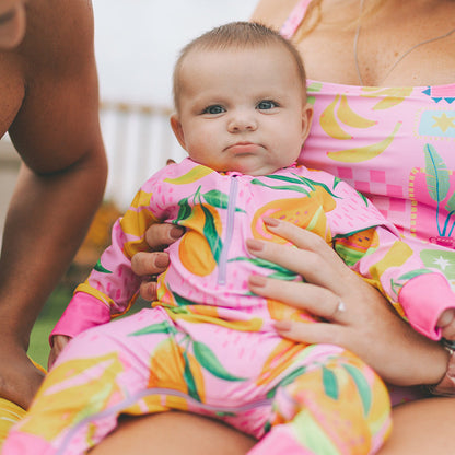 Baby in colorful outfit being held by a woman with a blurred background