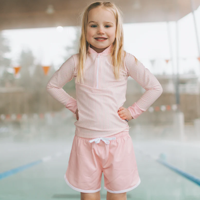 Young girl in a pink outfit standing in an indoor pool area