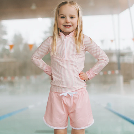 Young girl in a pink outfit standing in an indoor pool area