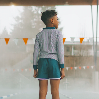 Person wearing a striped shirt and navy swim shorts standing in an indoor pool area.